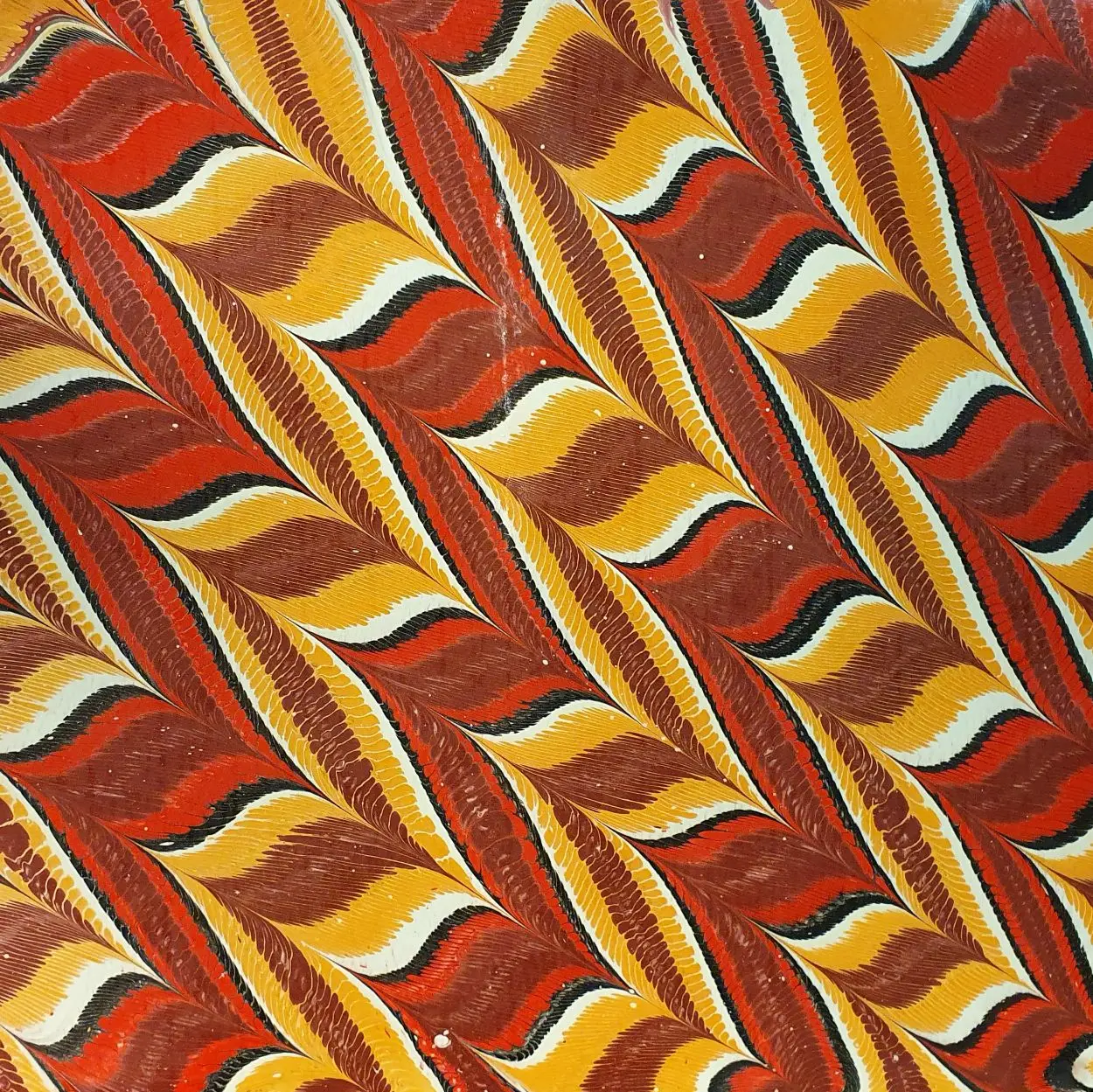 Marmoriertes Papier mit dynamischem Zickzackmuster in Rot- und Gelbtönen, klassische Marmoriertechnik